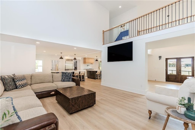 living room with french doors, a towering ceiling, and light wood-type flooring