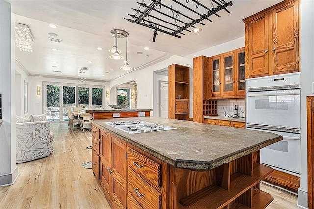 kitchen featuring stainless steel gas stovetop, backsplash, light wood-type flooring, double oven, and a center island