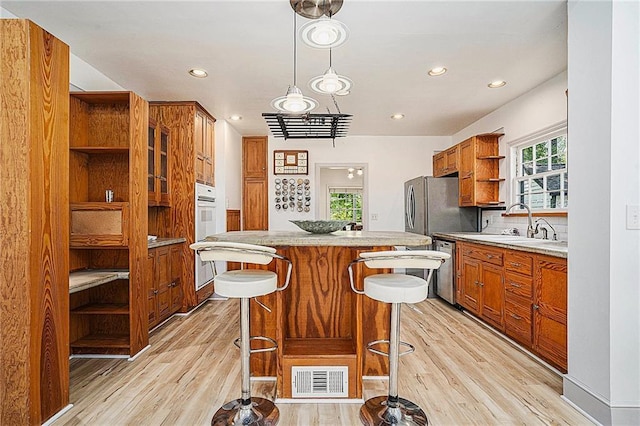 kitchen featuring decorative light fixtures, stainless steel appliances, sink, light hardwood / wood-style flooring, and a breakfast bar area