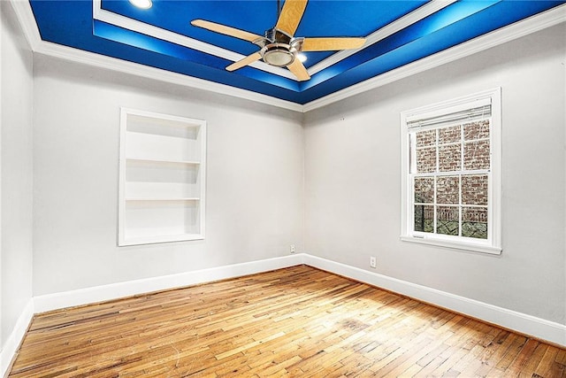 unfurnished room with built in shelves, ornamental molding, light wood-type flooring, ceiling fan, and a tray ceiling