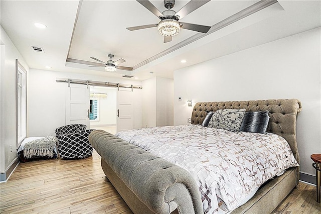 bedroom featuring ceiling fan, a barn door, hardwood / wood-style flooring, and a tray ceiling