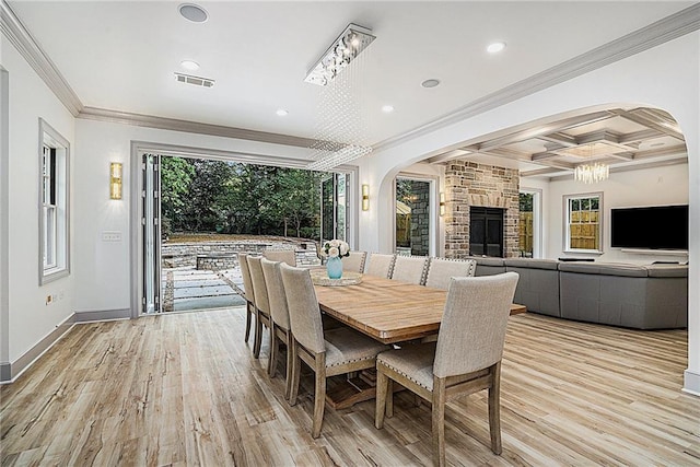 dining area with coffered ceiling, a stone fireplace, light wood-type flooring, crown molding, and beam ceiling