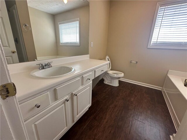 bathroom with baseboards, toilet, wood finished floors, a textured ceiling, and a bath