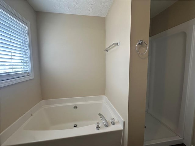 full bathroom featuring a textured ceiling, a stall shower, and a bath