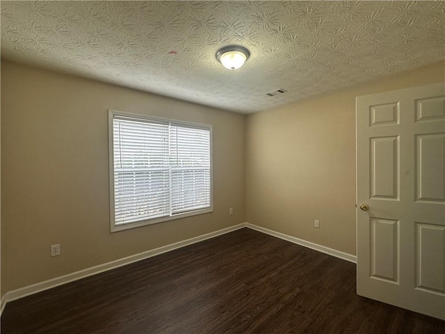 empty room with dark wood-style floors, visible vents, a textured ceiling, and baseboards