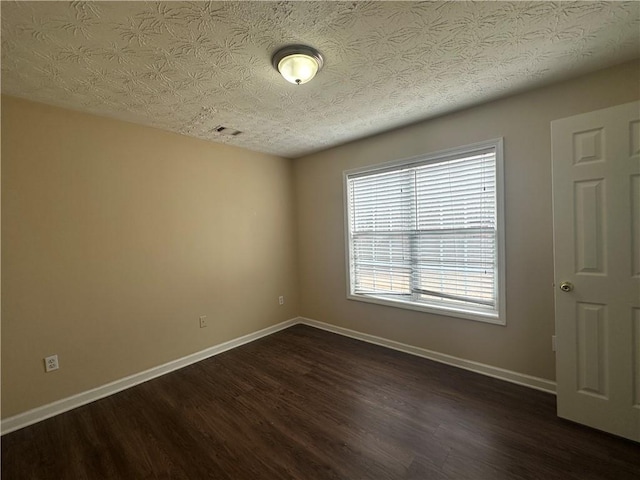 unfurnished room featuring dark wood-style floors, visible vents, a textured ceiling, and baseboards