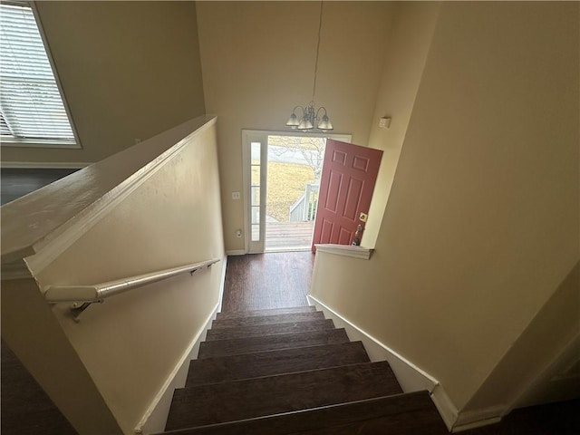 stairway with a notable chandelier, a towering ceiling, baseboards, and wood finished floors