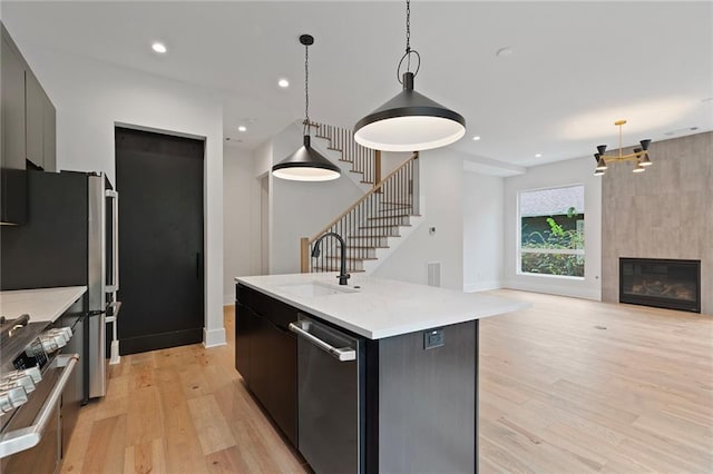 kitchen with sink, stainless steel appliances, decorative light fixtures, a kitchen island with sink, and a fireplace