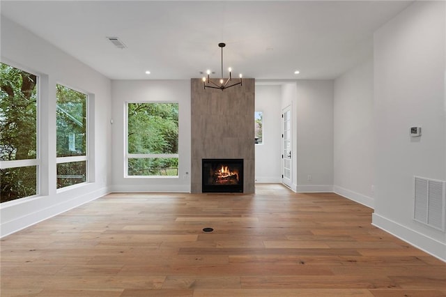 unfurnished living room with a fireplace, light wood-type flooring, a healthy amount of sunlight, and a notable chandelier