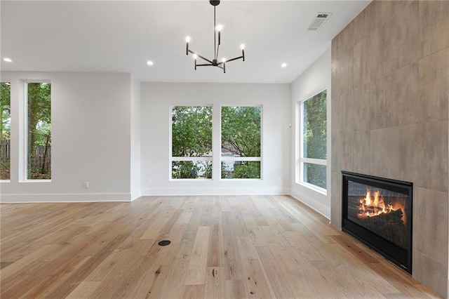 unfurnished living room featuring a notable chandelier, a tile fireplace, and light hardwood / wood-style flooring