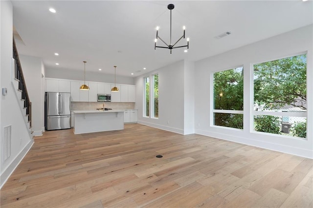 kitchen featuring light hardwood / wood-style floors, stainless steel appliances, hanging light fixtures, and an island with sink