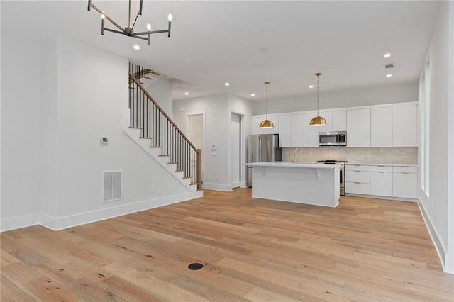 kitchen with white cabinets, appliances with stainless steel finishes, light hardwood / wood-style floors, and pendant lighting