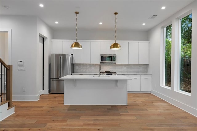 kitchen featuring light hardwood / wood-style flooring, an island with sink, decorative light fixtures, white cabinetry, and stainless steel appliances