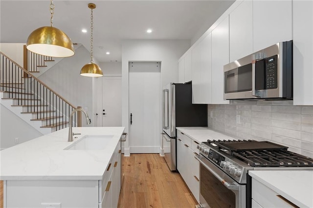 kitchen featuring stainless steel appliances, a kitchen island with sink, sink, pendant lighting, and light hardwood / wood-style flooring