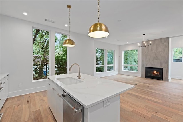 kitchen featuring stainless steel dishwasher, sink, white cabinetry, plenty of natural light, and an island with sink