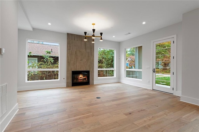 unfurnished living room featuring a large fireplace, light hardwood / wood-style flooring, and an inviting chandelier