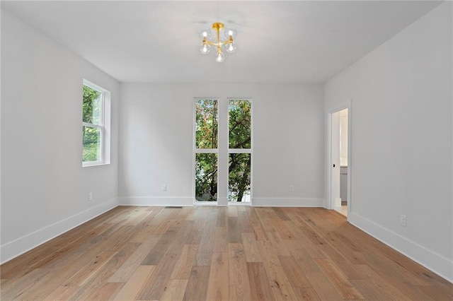 unfurnished room featuring a wealth of natural light, light hardwood / wood-style floors, and a notable chandelier