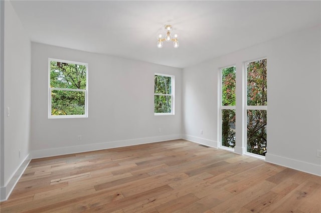 spare room featuring a healthy amount of sunlight, light wood-type flooring, and an inviting chandelier