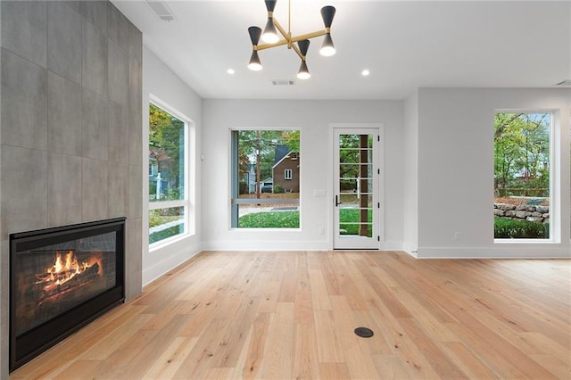 unfurnished living room with a fireplace, a chandelier, and light wood-type flooring