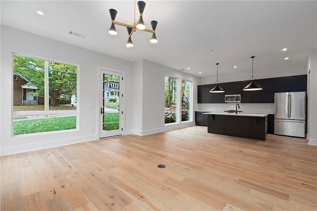 kitchen with plenty of natural light, stainless steel appliances, decorative light fixtures, and light wood-type flooring