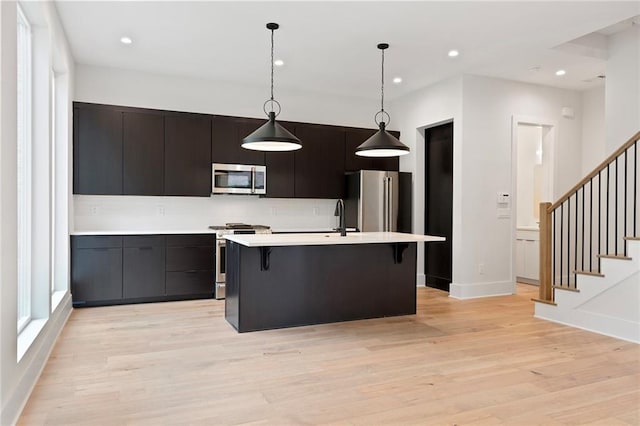 kitchen featuring stainless steel appliances, pendant lighting, a kitchen island with sink, a breakfast bar, and light wood-type flooring