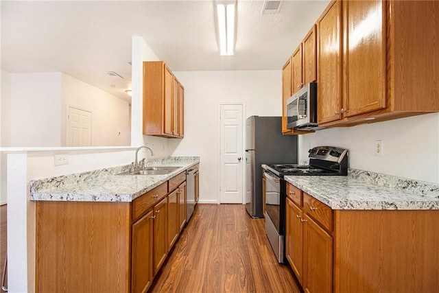 kitchen with sink, appliances with stainless steel finishes, dark hardwood / wood-style floors, light stone counters, and kitchen peninsula