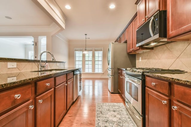 kitchen with stainless steel appliances, a sink, decorative columns, decorative backsplash, and dark stone countertops