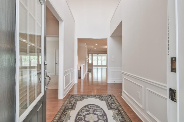 corridor featuring a decorative wall, wood finished floors, and wainscoting