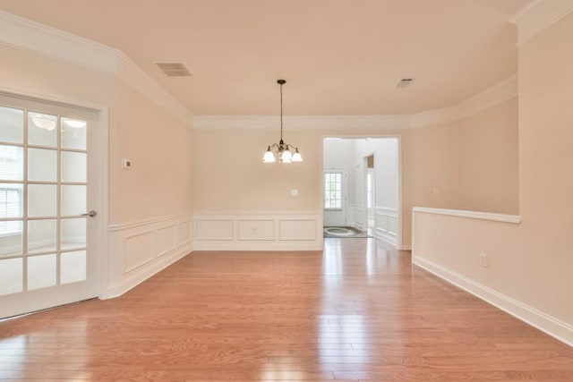 unfurnished room featuring a chandelier, light wood-style floors, ornamental molding, a wainscoted wall, and a decorative wall