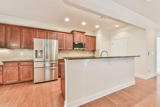 kitchen with stainless steel appliances, a breakfast bar, light wood-type flooring, a kitchen island with sink, and crown molding