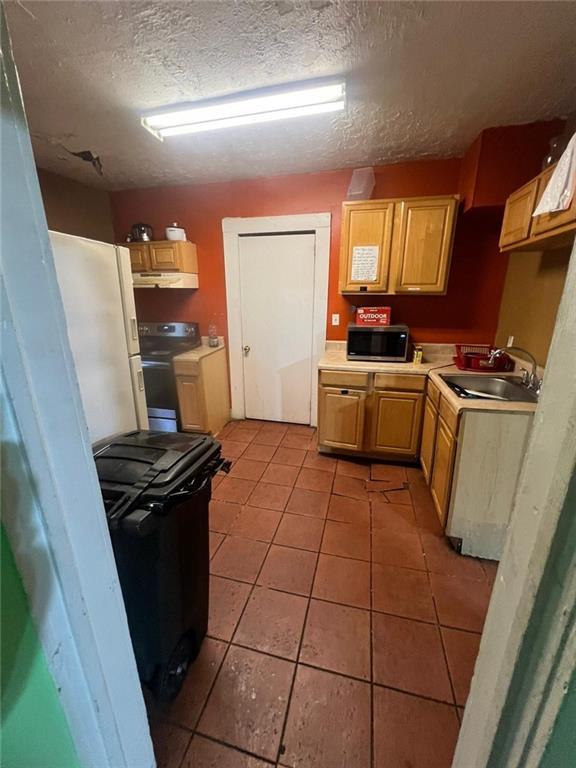 kitchen with appliances with stainless steel finishes, light brown cabinetry, sink, light tile patterned floors, and a textured ceiling