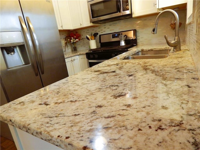 kitchen with appliances with stainless steel finishes, tasteful backsplash, light stone counters, sink, and white cabinetry