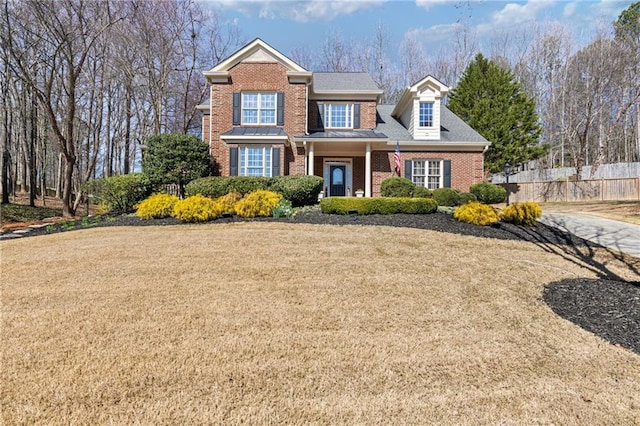 traditional home featuring a front yard, fence, and brick siding