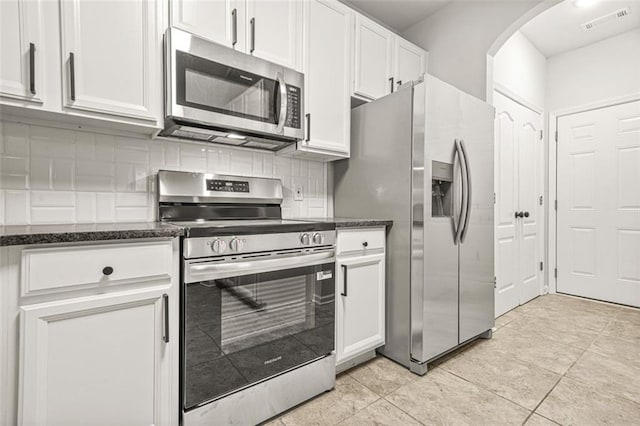 6571 Splitpine Ct, Atlanta, GA 30349 - kitchen featuring stainless steel appliances, arched walkways, white cabinetry, and dark stone counters