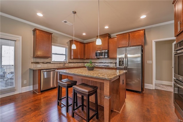 kitchen with brown cabinetry, dark wood finished floors, ornamental molding, stainless steel appliances, and a sink