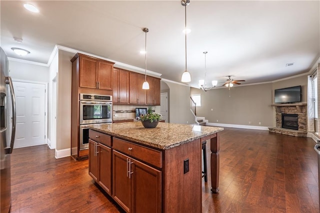 kitchen featuring light stone countertops, dark wood-style flooring, a fireplace, a center island, and pendant lighting