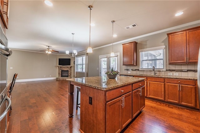 kitchen with brown cabinets, visible vents, backsplash, dark wood-type flooring, and a stone fireplace