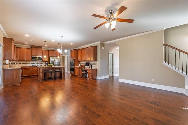 kitchen with baseboards, arched walkways, dark wood-style floors, appliances with stainless steel finishes, and brown cabinets