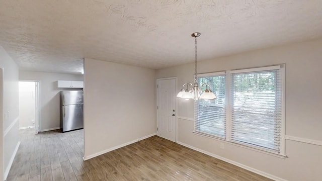 unfurnished dining area featuring a textured ceiling, baseboards, light wood-style flooring, and a chandelier