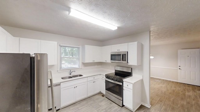 kitchen with appliances with stainless steel finishes, a sink, light countertops, light wood-style floors, and a textured ceiling