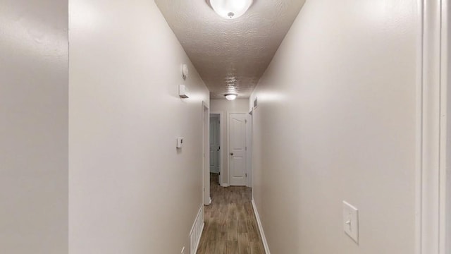 hallway with wood finished floors, baseboards, and a textured ceiling