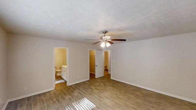 unfurnished bedroom featuring baseboards, light wood-type flooring, a spacious closet, ensuite bathroom, and a ceiling fan