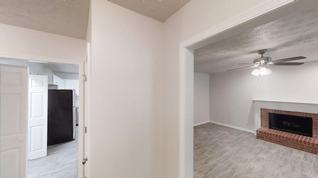 hall with light wood finished floors, a textured ceiling, and baseboards