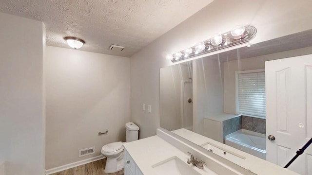 bathroom featuring toilet, a textured ceiling, wood finished floors, vanity, and a tub