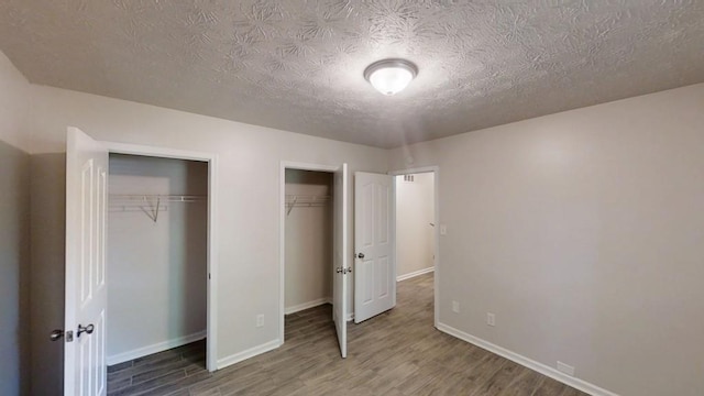 unfurnished bedroom featuring wood finished floors, two closets, a textured ceiling, and baseboards