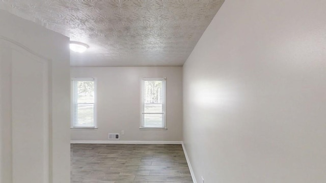 spare room with a textured ceiling, wood finished floors, and baseboards