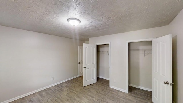 unfurnished bedroom with wood finished floors, two closets, baseboards, and a textured ceiling