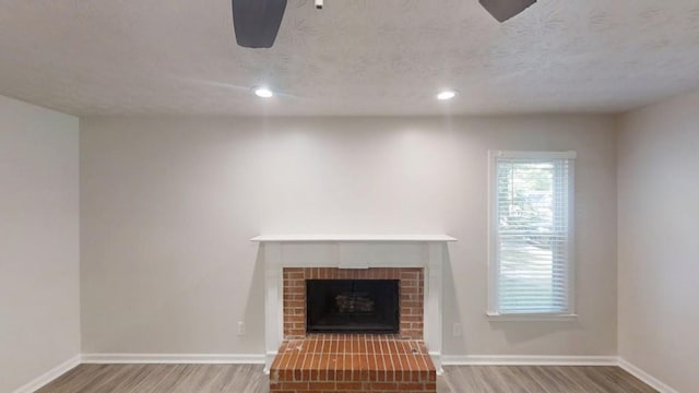 unfurnished living room with wood finished floors, a fireplace, baseboards, recessed lighting, and a textured ceiling