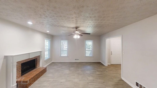 unfurnished living room featuring ceiling fan, baseboards, a fireplace, wood finished floors, and a textured ceiling