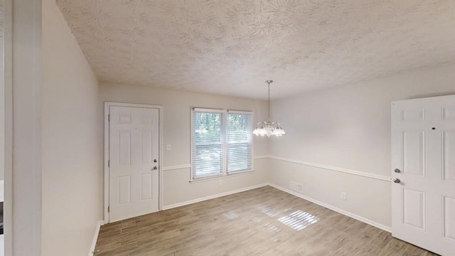 foyer with a textured ceiling, a chandelier, wood finished floors, and baseboards